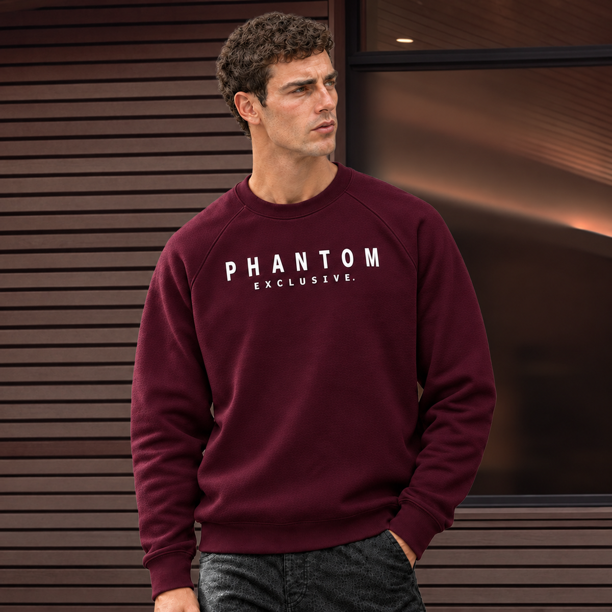 A man wearing a maroon crewneck sweatshirt with 'PHANTOM EXCLUSIVE' printed in white across the chest, posed against a modern dark wood-paneled wall.